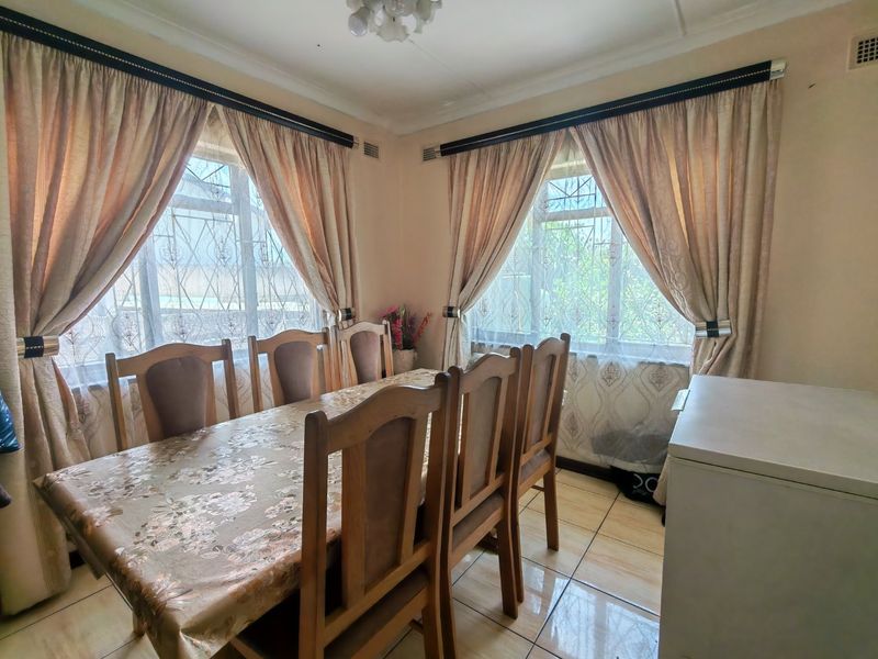 A functional dining room featuring tiled flooring and large windows with security bars, providing natural light to the space.