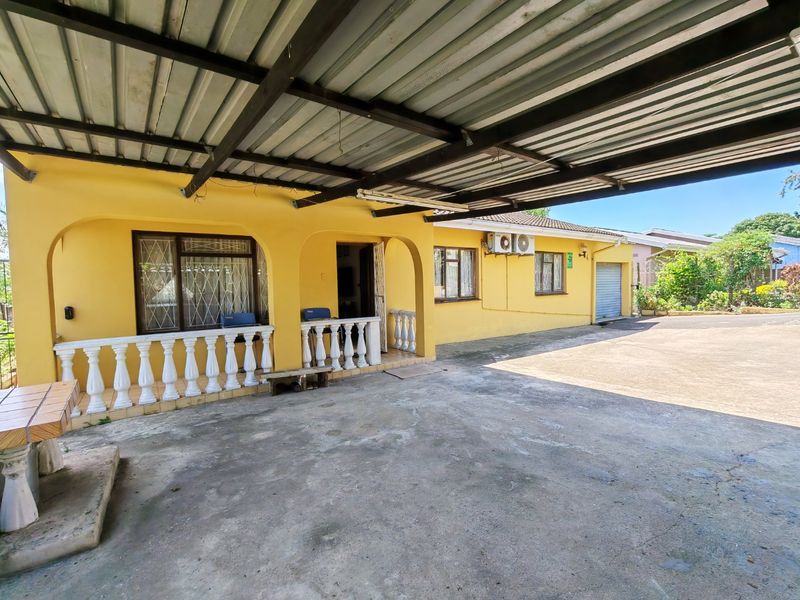 Front exterior view of the house featuring a large covered carport, concrete driveway, and yellow facade with security features.