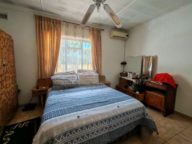 A bedroom featuring tiled flooring, a ceiling fan, and a wall-mounted air conditioning unit, with visible signs of wear on the ceiling.