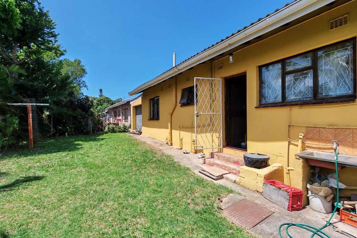 Rear view of the property featuring a lawn, concrete pathway, external sink, and security gate access to the main building.