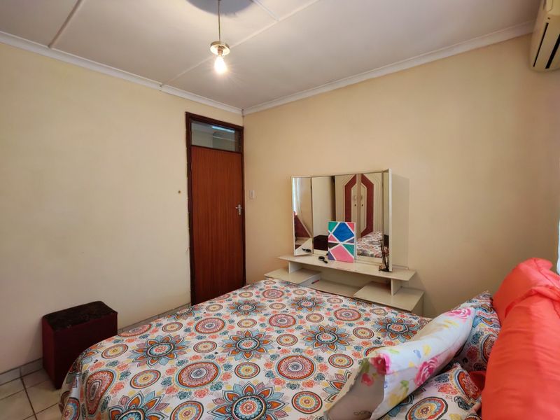 A functional bedroom featuring tiled flooring, a timber door, and a wall-mounted air conditioning unit.