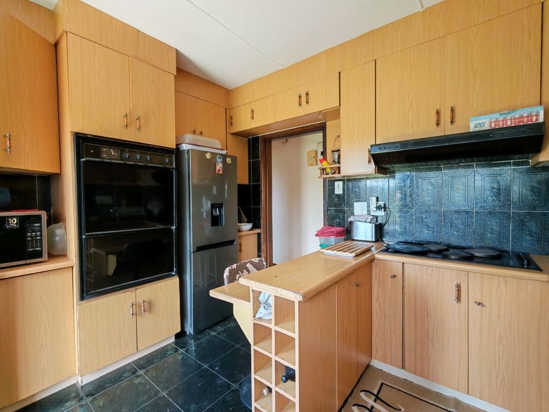 A functional kitchen featuring wood-look cabinetry, a built-in oven, a hob with an extractor fan, and dark tiled flooring.