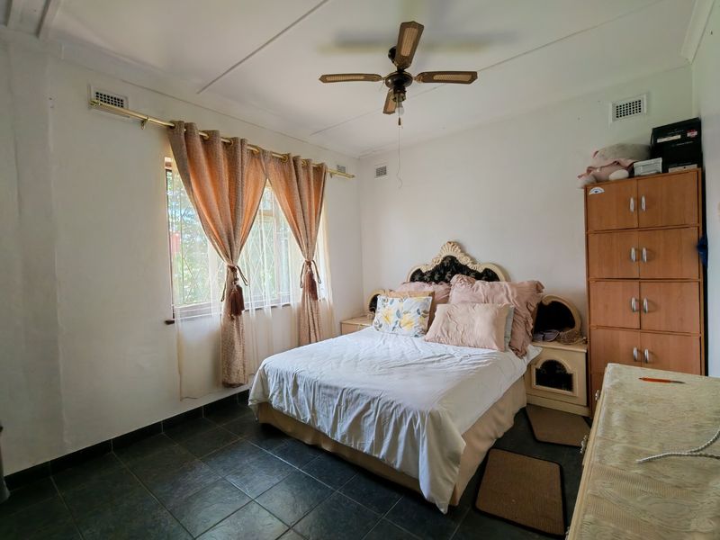 A functional bedroom featuring dark tiled flooring, a ceiling fan, and built-in storage cabinetry, offering a neutral base for potential updates.