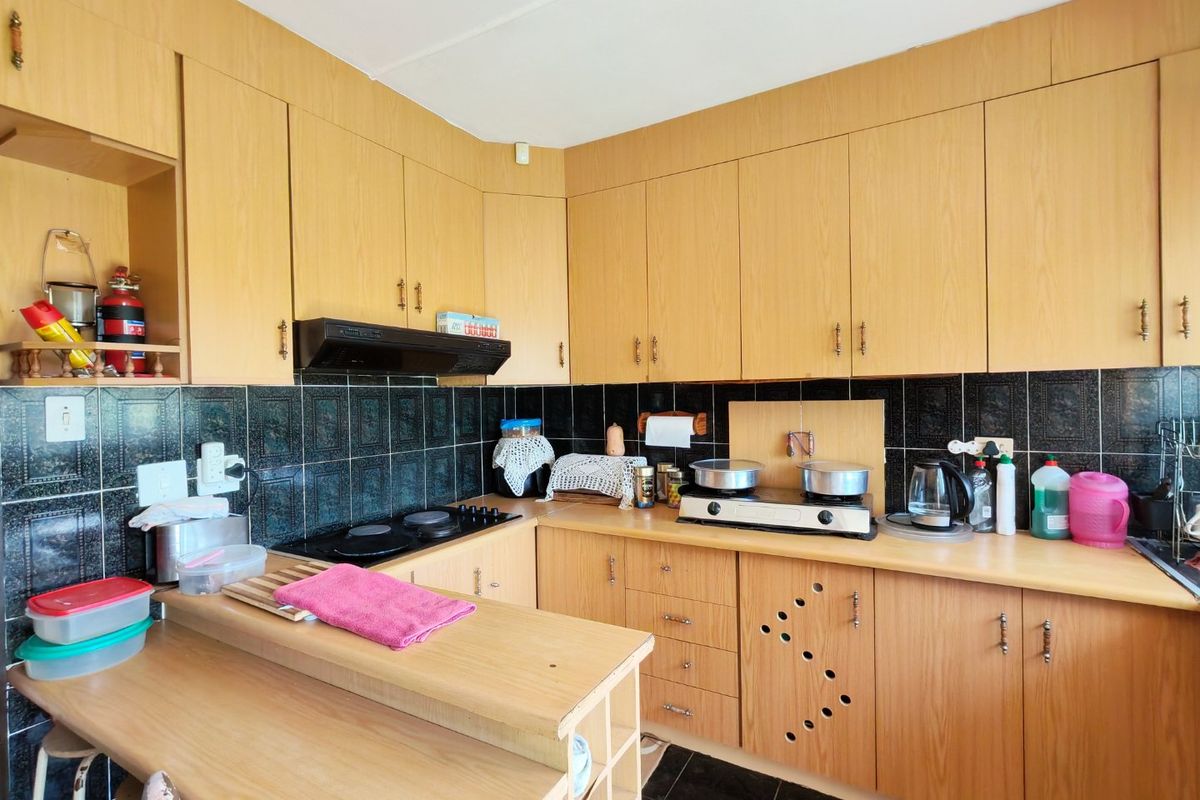 A functional kitchen featuring light wood-look cabinetry, dark tiled backsplash, and integrated hob with extractor fan, offering a classic dated aesthetic.