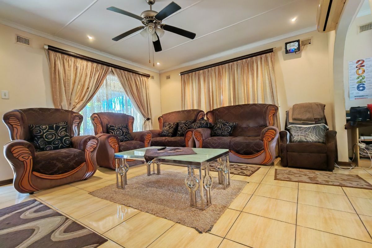 A spacious living room featuring ceramic floor tiles, a ceiling fan, and a wall-mounted air conditioning unit.