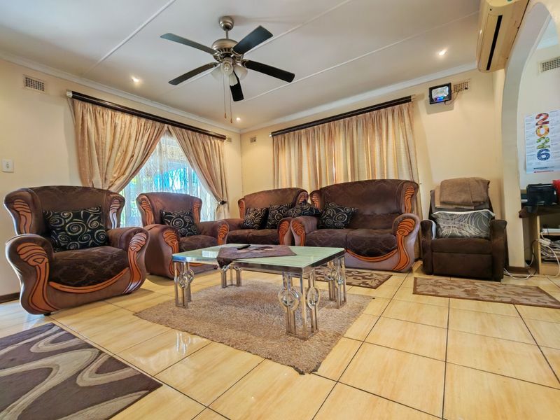 A spacious living room featuring ceramic floor tiles, a ceiling fan, and a wall-mounted air conditioning unit.