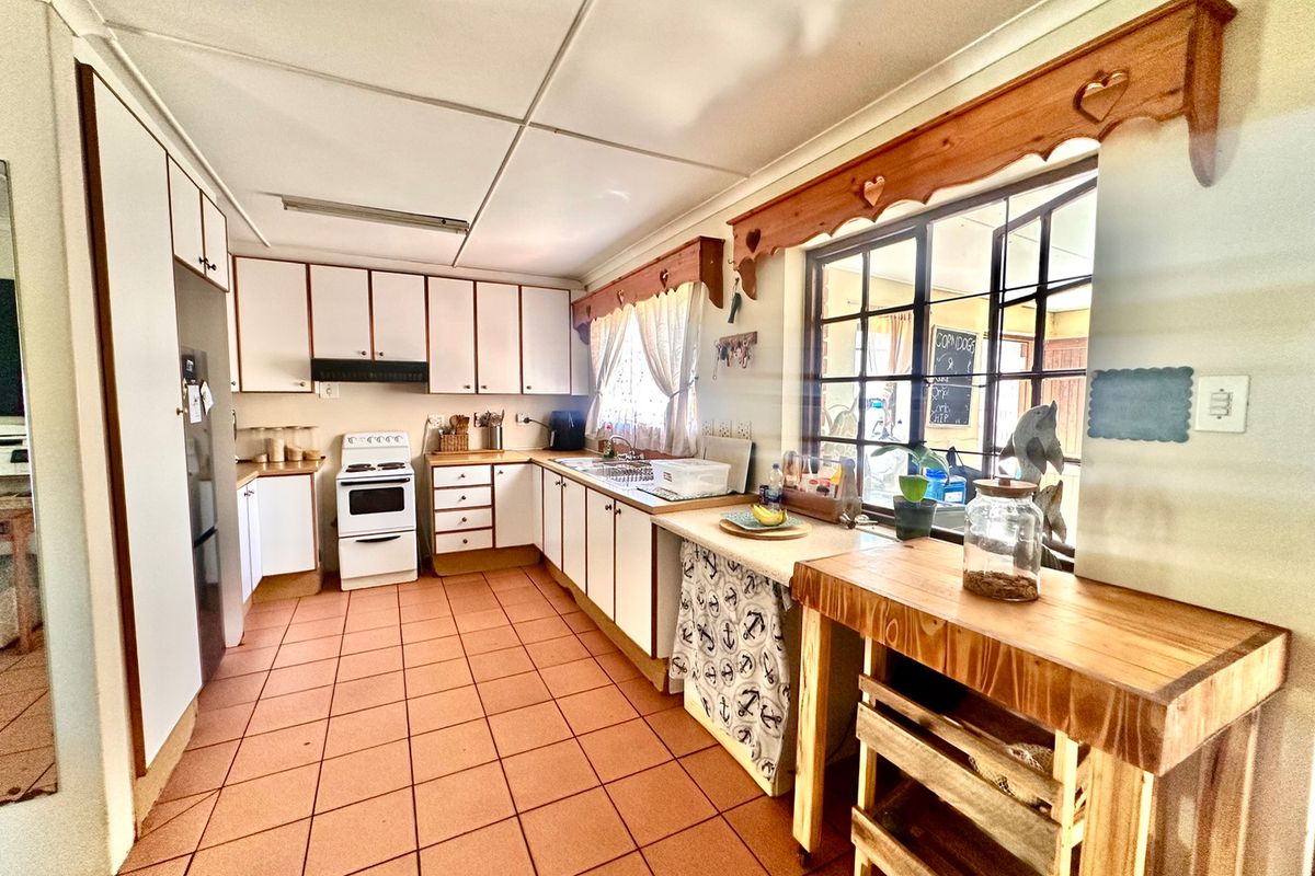 A functional kitchen featuring white cabinetry, tiled flooring, a freestanding stove, and timber window pelmets, offering a classic layout with potential for modern updates.