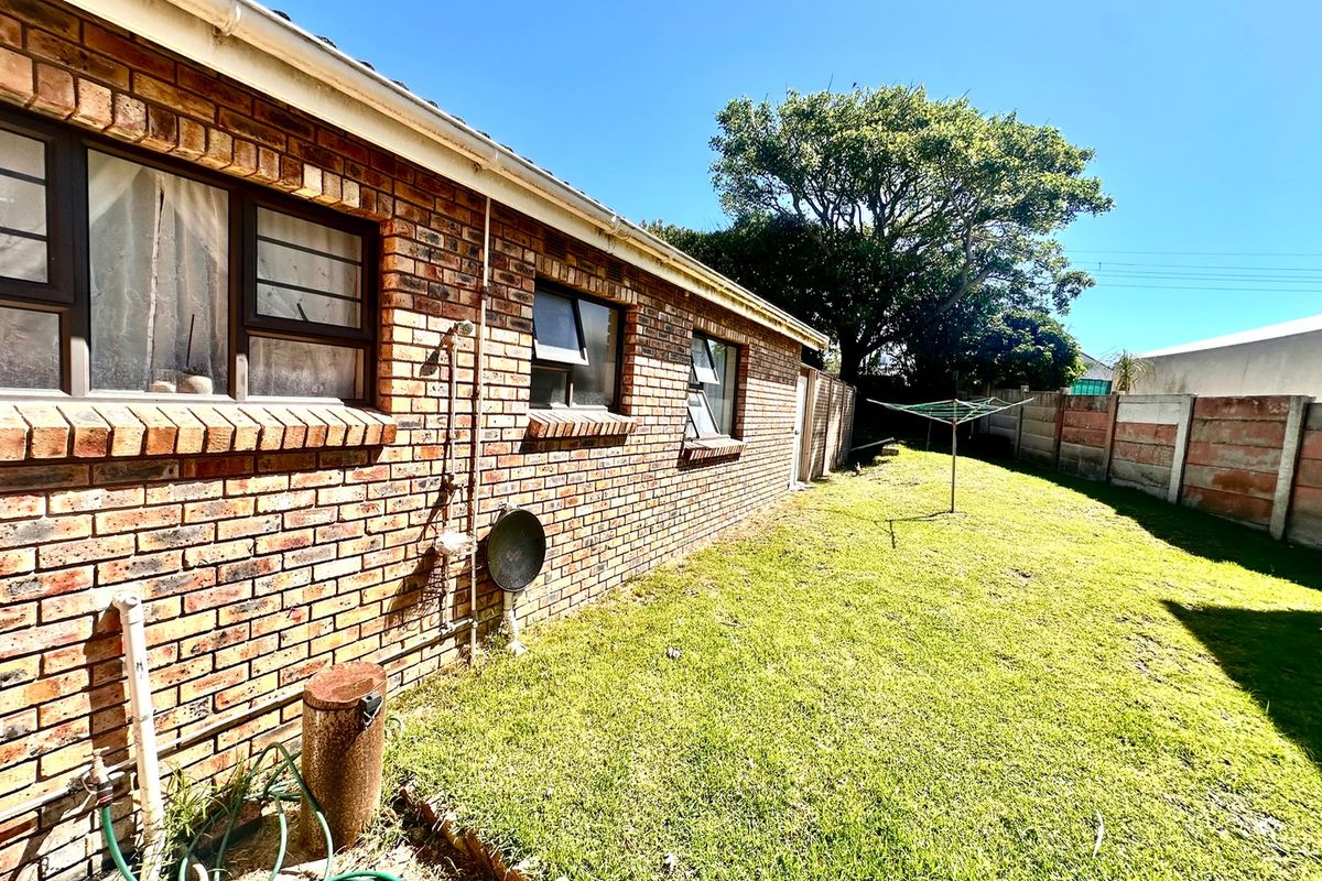 Rear exterior view of the property featuring a brick facade, aluminium window frames, and a private garden area with a precast concrete boundary wall.