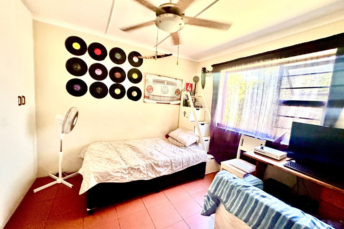 A functional bedroom featuring tiled flooring, a ceiling fan, and security bars on the window.
