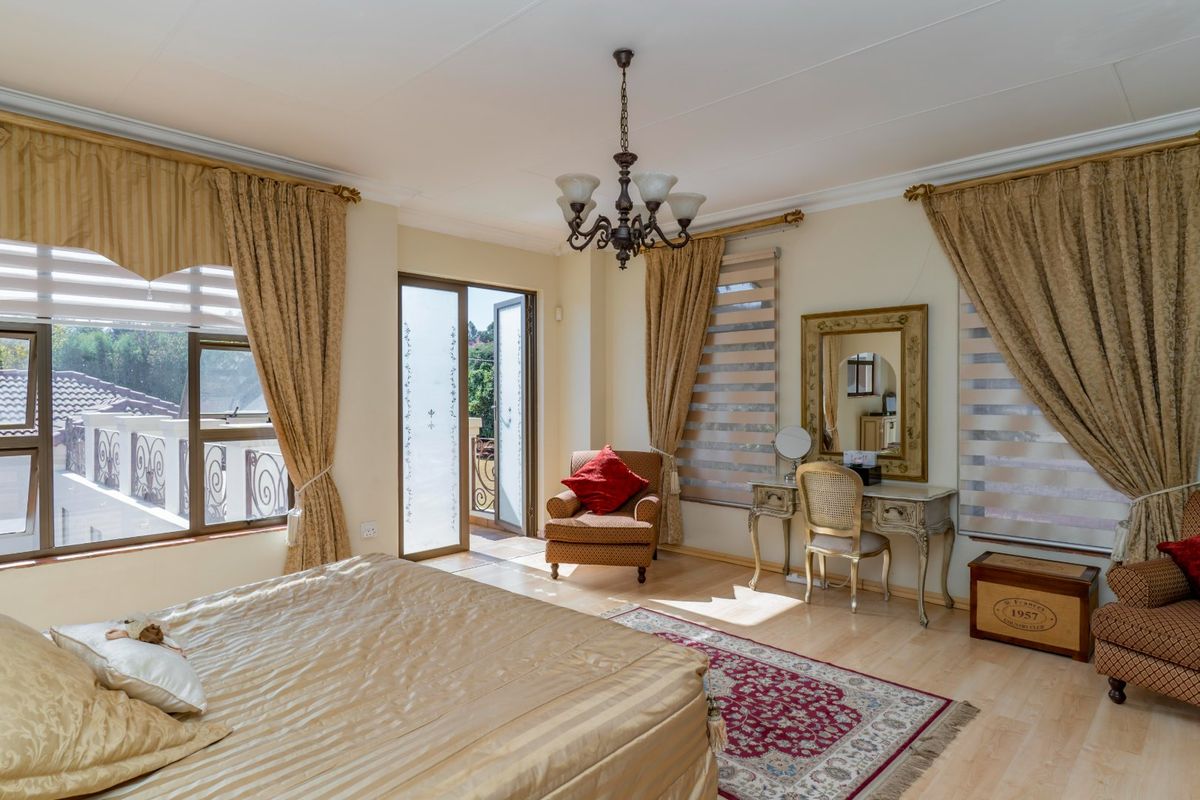 Spacious bedroom featuring laminate flooring, a classic chandelier, and direct access to a private balcony through sliding glass doors.