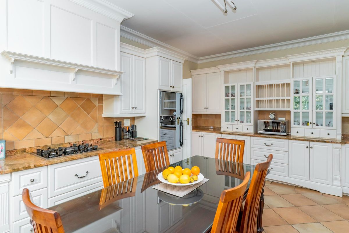 A classic kitchen featuring white cabinetry, granite countertops, a gas hob, and integrated oven, complemented by tiled flooring and decorative crown molding.