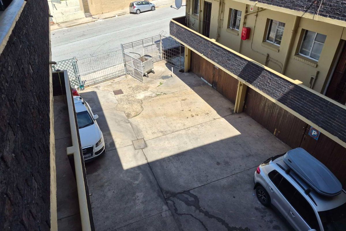An elevated view of the apartment complex parking area featuring concrete paving, secure gated access, and integrated garage units.