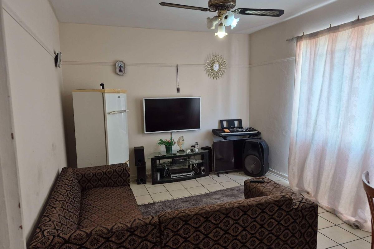 A living room featuring tiled flooring, a ceiling fan with integrated lighting, and large windows with curtains.