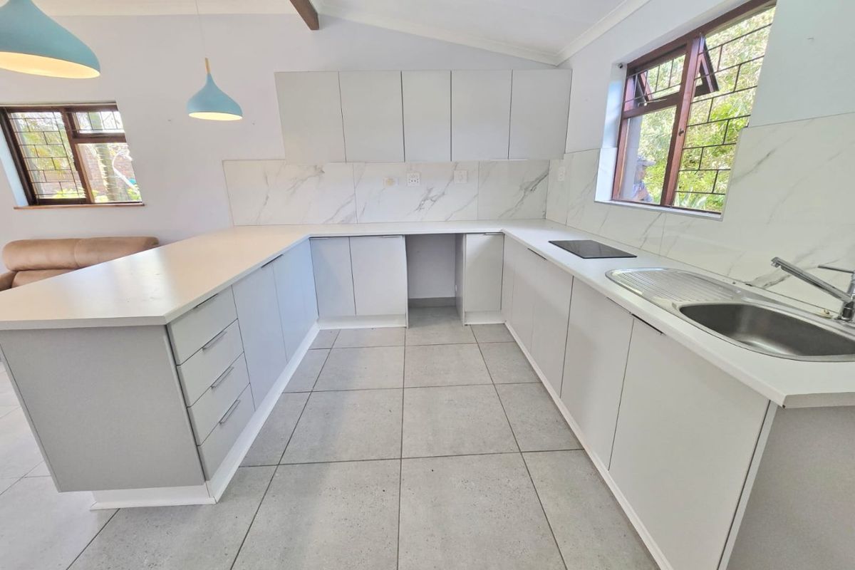 Modern kitchen featuring light grey cabinetry, marble-look splashbacks, tiled flooring, and an integrated hob, offering a clean and functional workspace.