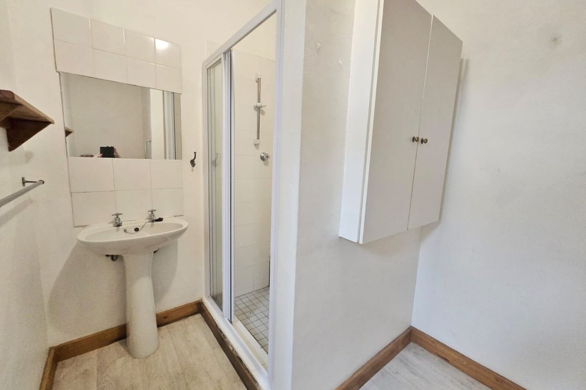 A functional bathroom featuring a pedestal basin, a shower enclosure with sliding doors, and built-in wall cabinetry.
