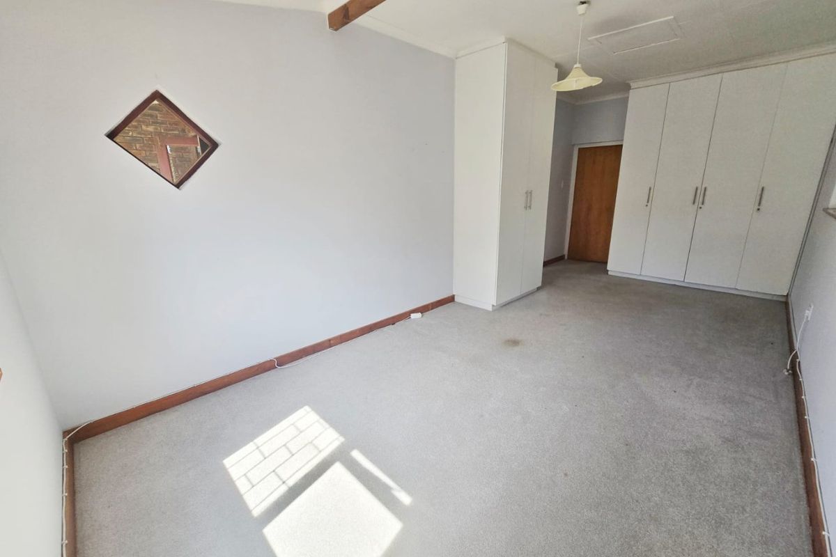 An empty bedroom featuring built-in cupboards, an exposed ceiling beam, and carpeted flooring, offering a blank canvas for personalization.