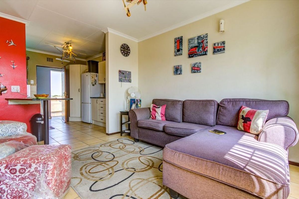 Open-plan living area featuring tiled floors, a breakfast bar, and an adjoining kitchen space with built-in cabinetry.