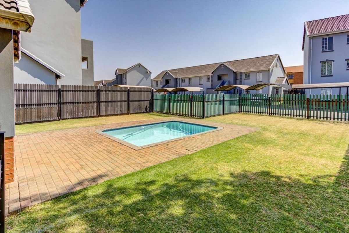 A communal outdoor area featuring a swimming pool with a paved surround and a grass lawn, enclosed by perimeter fencing.