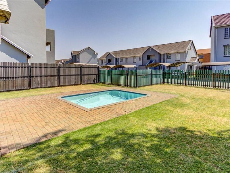 A communal outdoor area featuring a swimming pool with a paved surround and a grass lawn, enclosed by perimeter fencing.