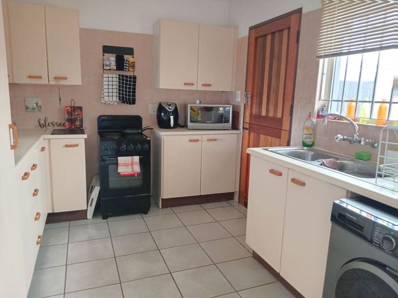 A functional kitchen featuring built-in cabinetry, tiled flooring, a stainless steel sink, and a window with security bars.