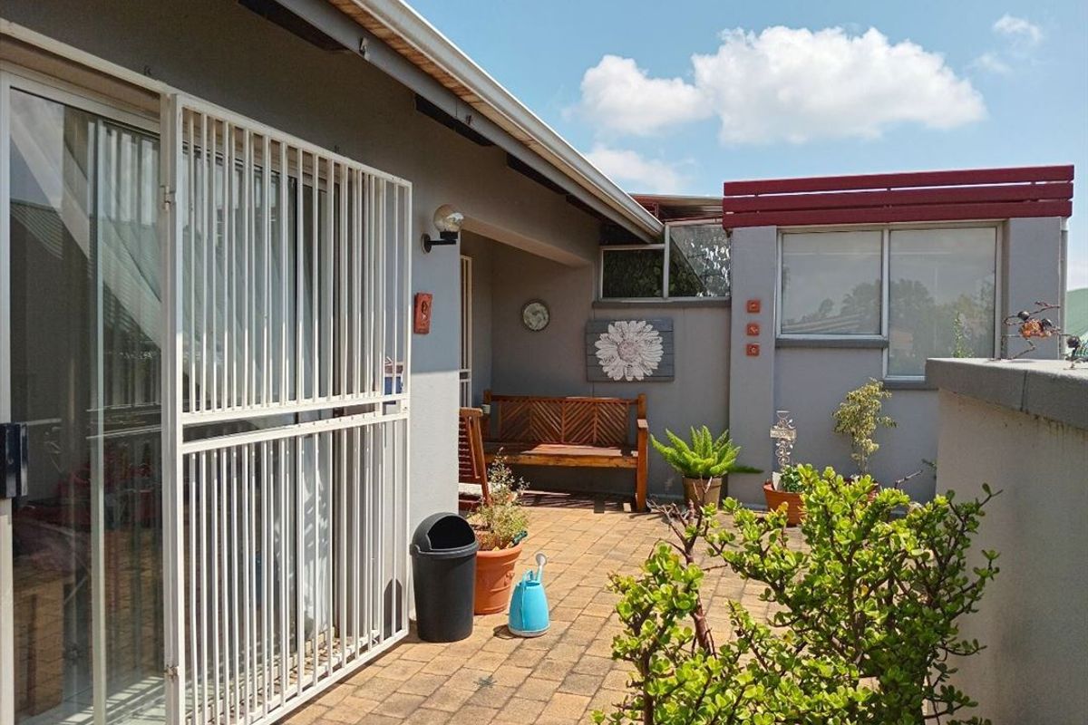 A paved outdoor patio area featuring a security gate, sliding glass door access, and a parapet wall, providing a functional private outdoor space.