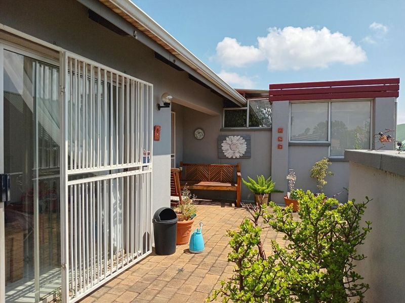 A paved outdoor patio area featuring a security gate, sliding glass door access, and a parapet wall, providing a functional private outdoor space.