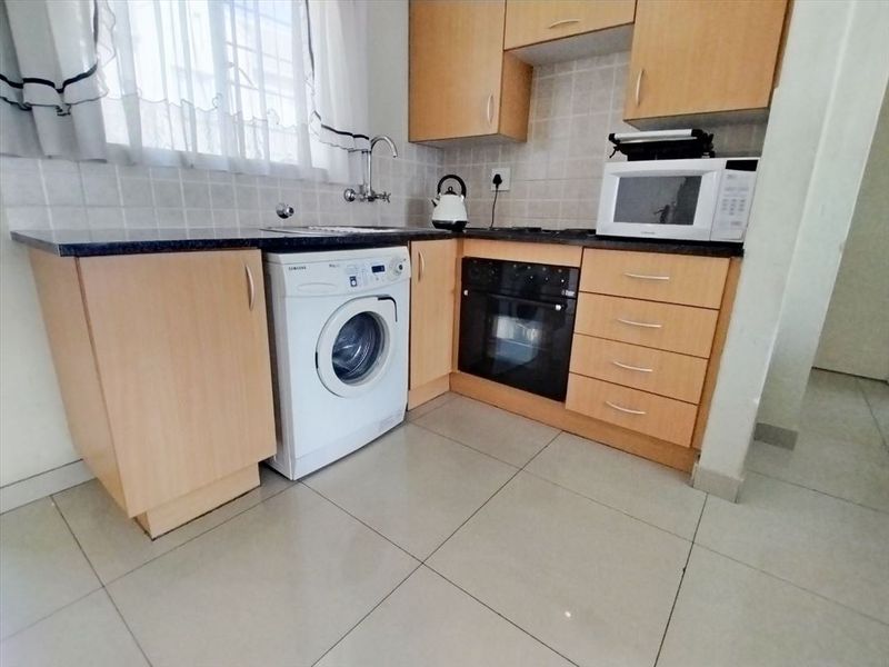 Compact kitchen featuring laminate cabinetry, granite countertops, built-in oven, hob, and tiled flooring with integrated laundry plumbing.