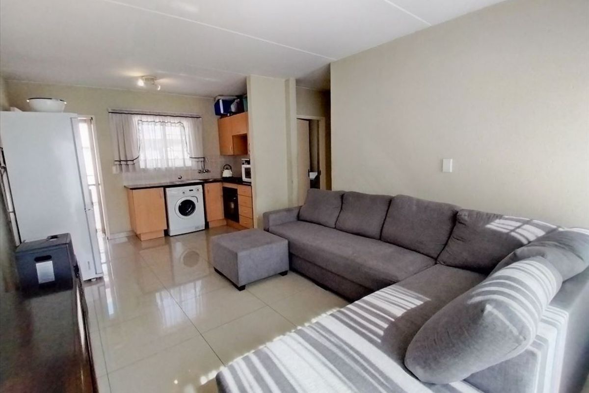 Open-plan living area featuring tiled flooring and a compact kitchen with built-in cabinetry, oven, and hob.