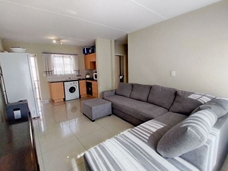 Open-plan living area featuring tiled flooring and a compact kitchen with built-in cabinetry, oven, and hob.