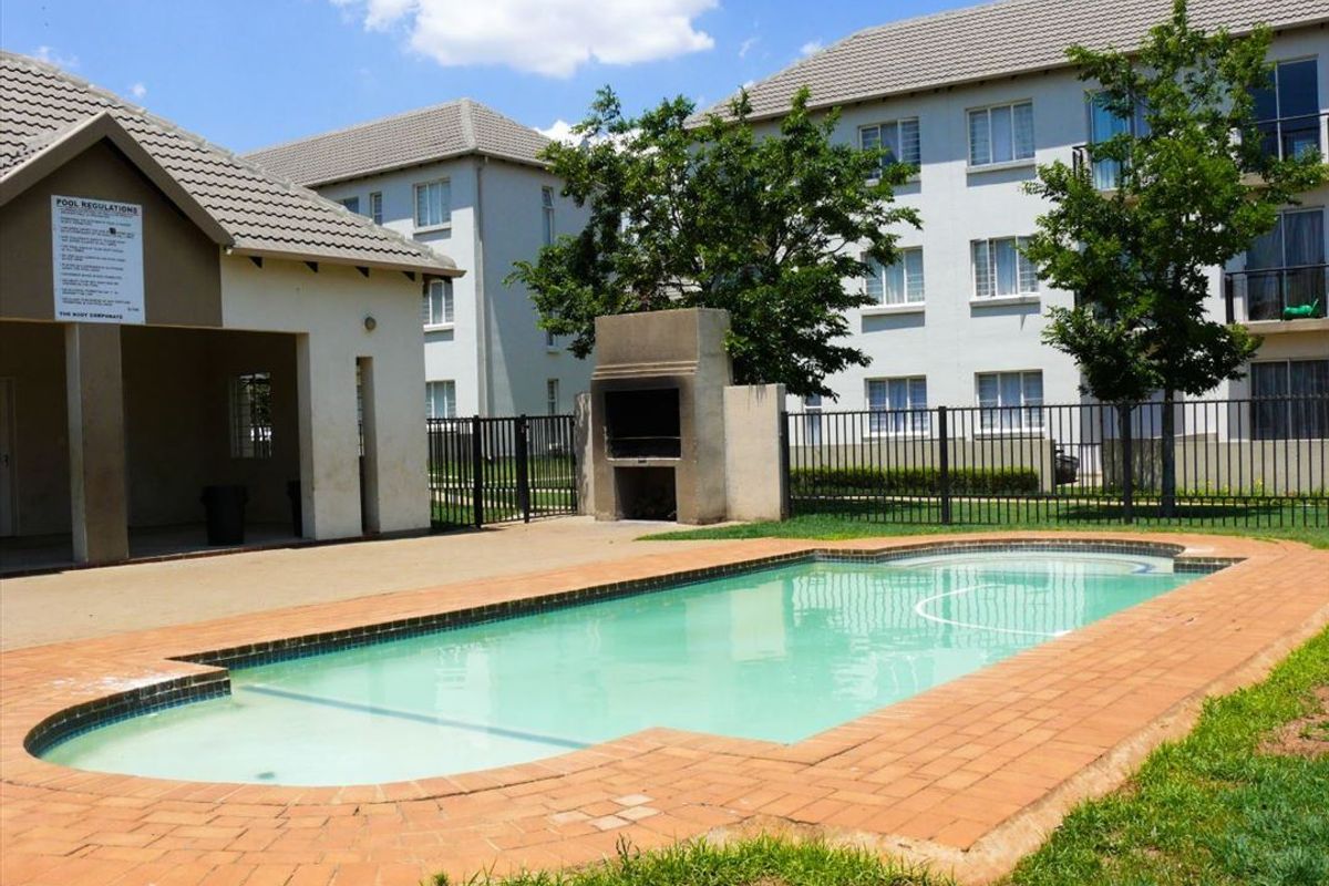 Communal swimming pool area featuring a built-in braai, covered patio space, and secure metal perimeter fencing within an apartment complex.
