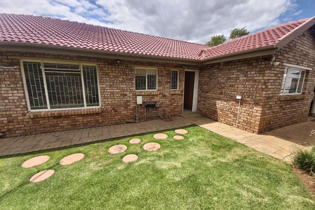 Rear view of the townhouse featuring a face brick facade, tiled roof, paved walkway, and a well-maintained lawn with a stone path.