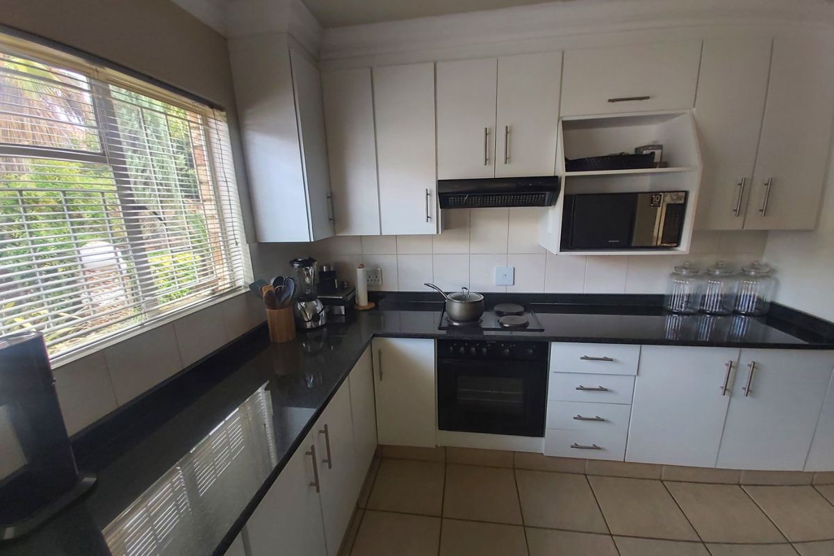 A functional kitchen featuring white cabinetry, dark granite countertops, built-in oven, electric hob, and tiled flooring with natural light from the side window.