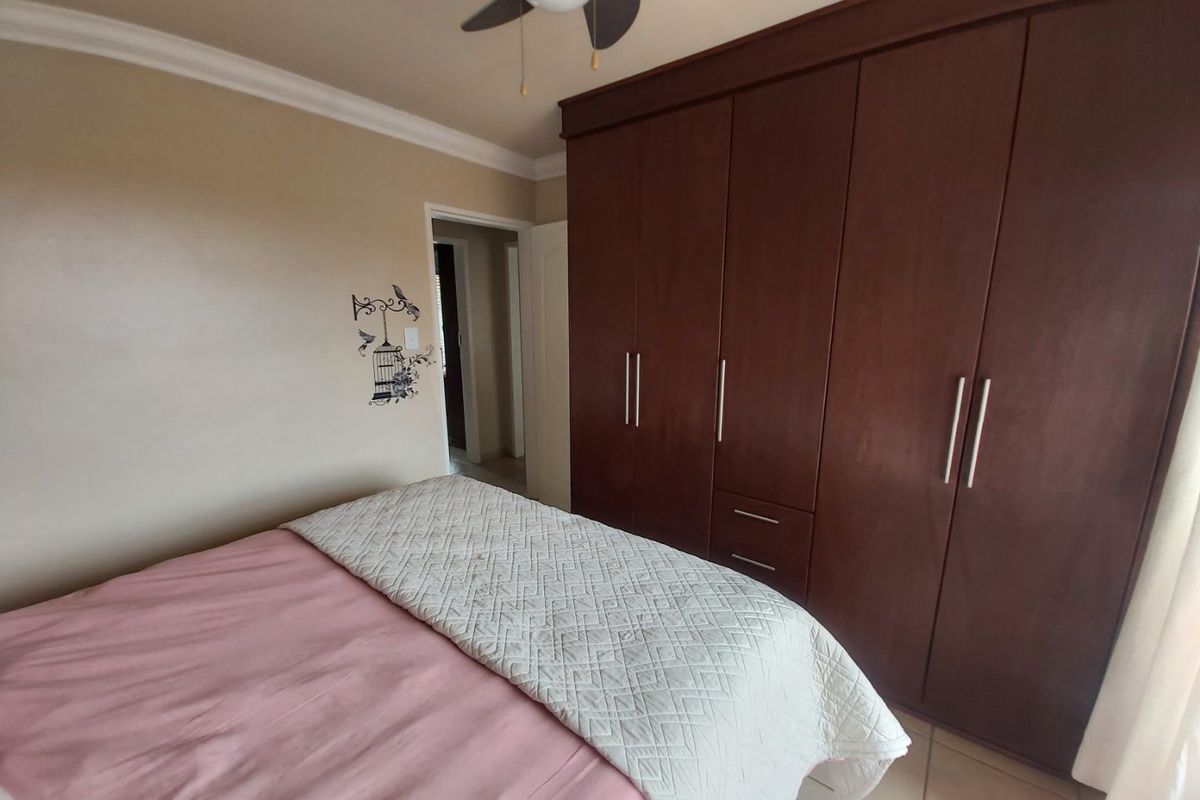 A bedroom featuring dark wood built-in cupboards, a ceiling fan, and tiled flooring.