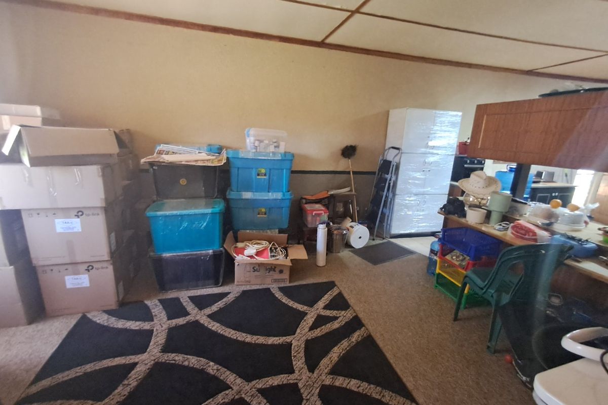 A living area featuring carpeted flooring and a suspended ceiling, currently used for storage.