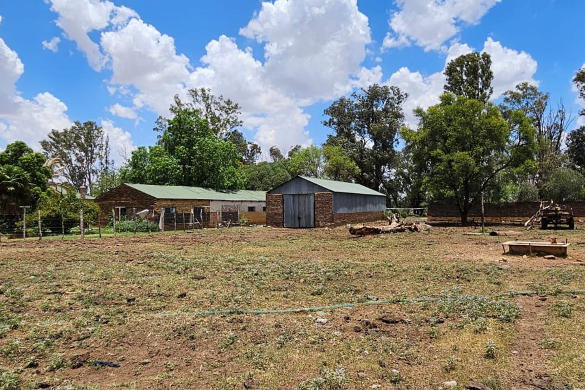 A view of the rear farm grounds featuring brick outbuildings with corrugated metal roofing and established perimeter fencing.