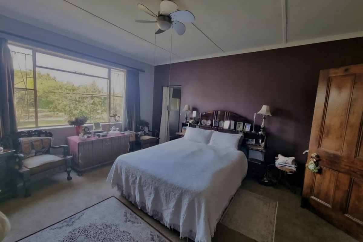 A spacious bedroom featuring a large window with natural light, a ceiling fan, and a solid wooden door.