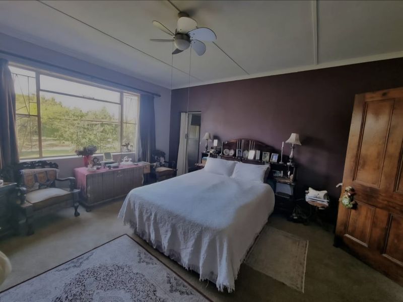 A spacious bedroom featuring a large window with natural light, a ceiling fan, and a solid wooden door.
