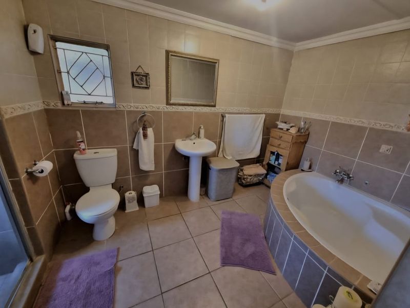 A functional bathroom featuring a pedestal basin, a built-in bathtub with tiled surround, and neutral wall and floor tiling.