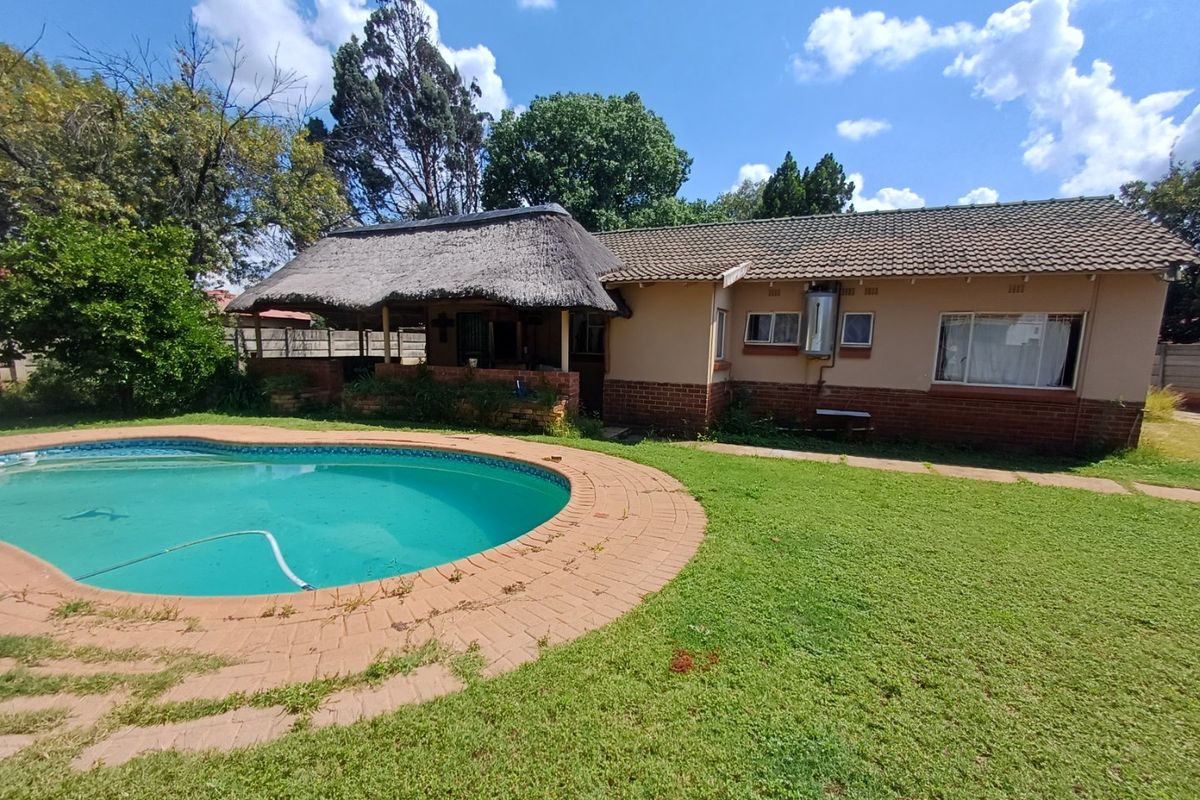 Rear exterior view featuring a swimming pool, brick paved surround, and a thatched roof lapa area set against the main house structure.