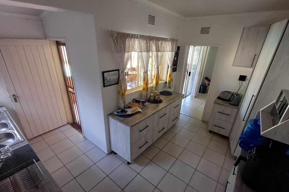 A functional kitchen featuring tiled flooring, built-in cabinetry, and a double sink, with direct access to adjacent living areas.