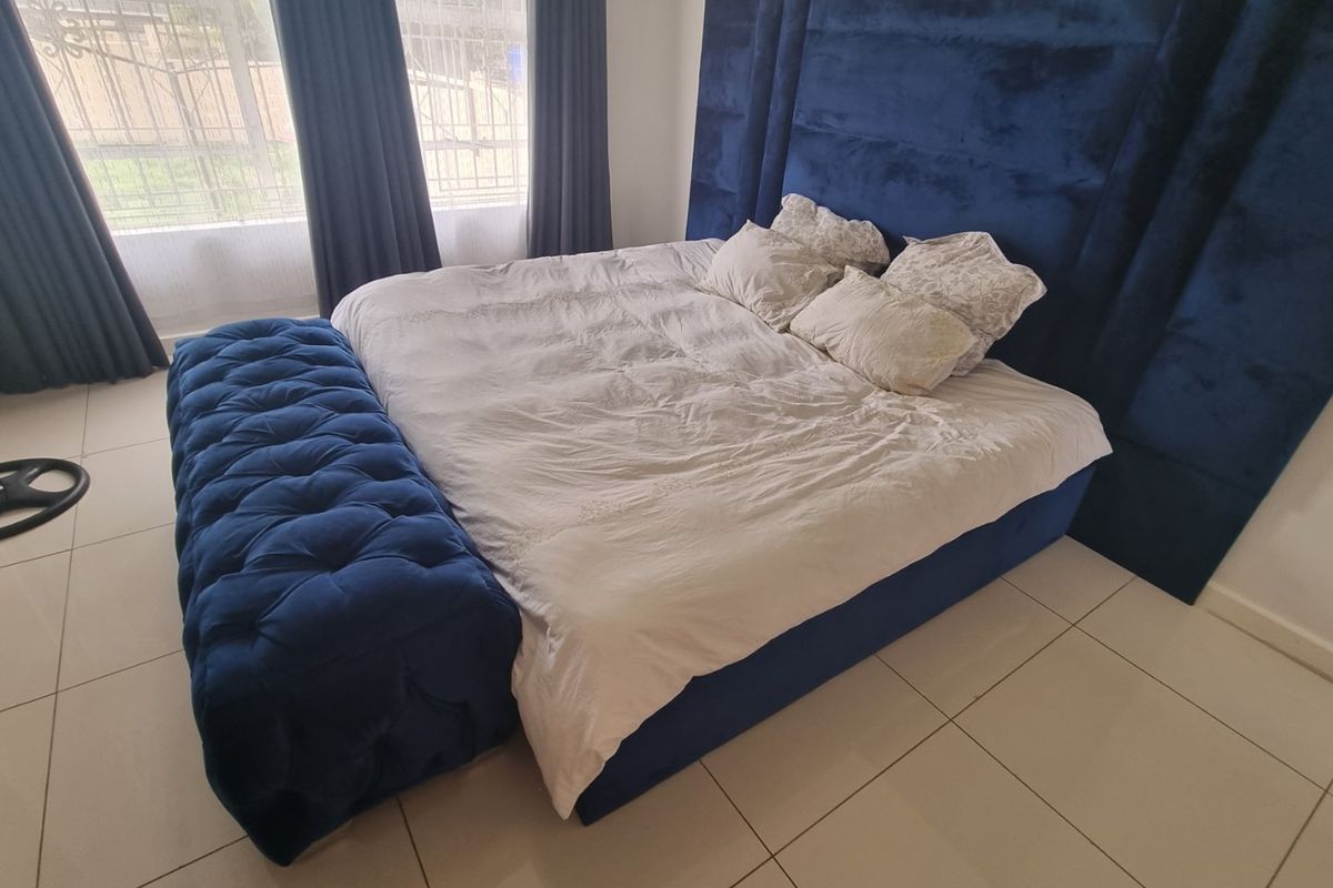 A well-lit bedroom featuring large windows with curtain tracks and neutral tiled flooring, providing a clean and functional living space.