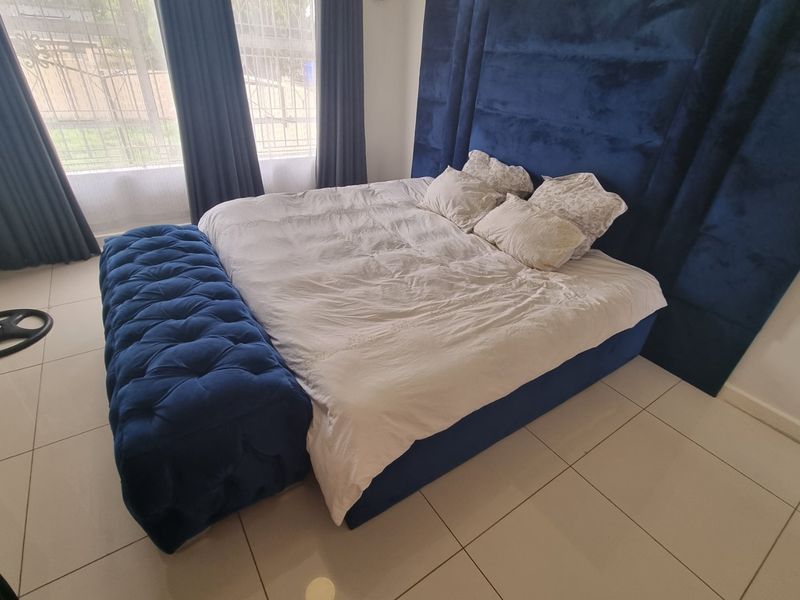 A well-lit bedroom featuring large windows with curtain tracks and neutral tiled flooring, providing a clean and functional living space.