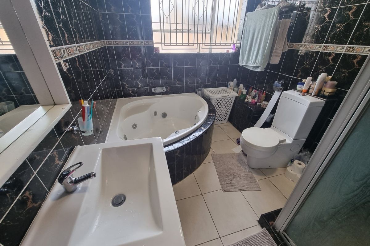 A bathroom featuring a corner spa bath, wall-mounted basin, and toilet, finished with dark patterned wall tiles and light floor tiles.
