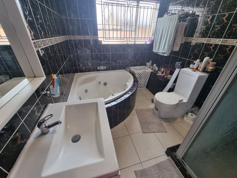 A bathroom featuring a corner spa bath, wall-mounted basin, and toilet, finished with dark patterned wall tiles and light floor tiles.