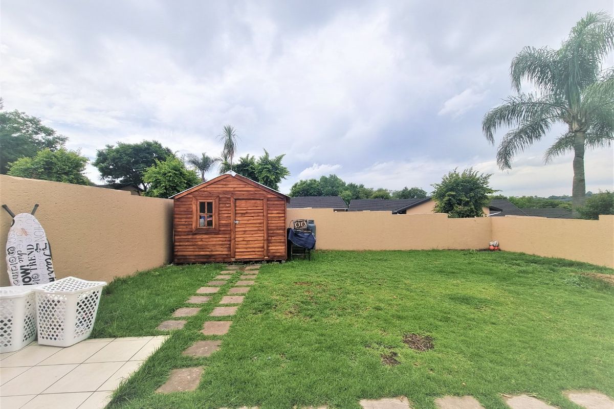 A private rear garden featuring a lawn, stone paver pathway, and a wooden storage shed enclosed by a perimeter boundary wall.