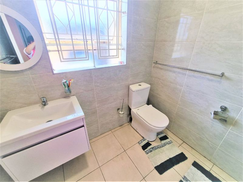 A modern, well-maintained bathroom featuring neutral wall and floor tiles, a vanity cabinet with basin, and a standard toilet.