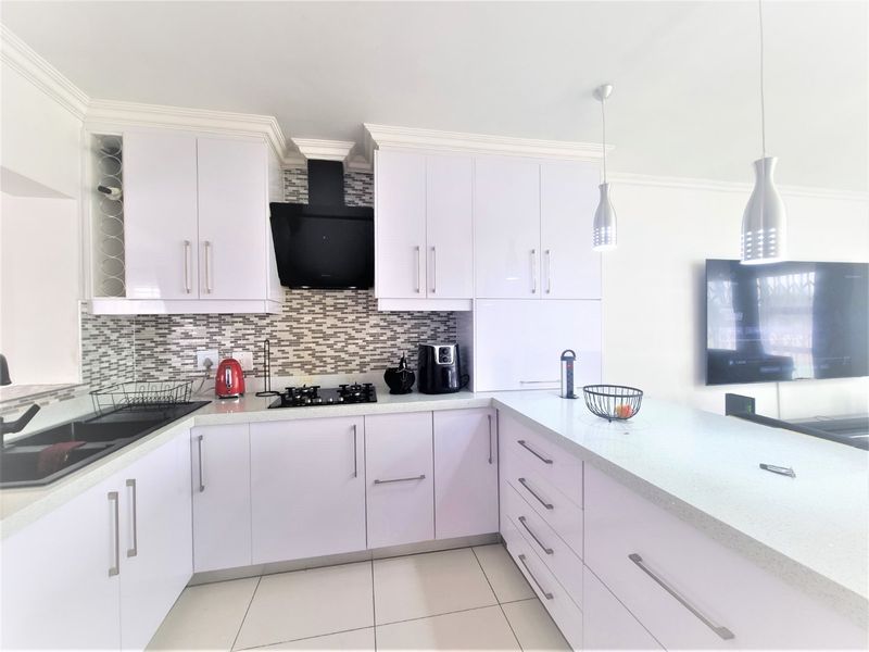Modern open-plan kitchen featuring white high-gloss cabinetry, stone countertops, a gas hob with extractor fan, and a breakfast bar area.