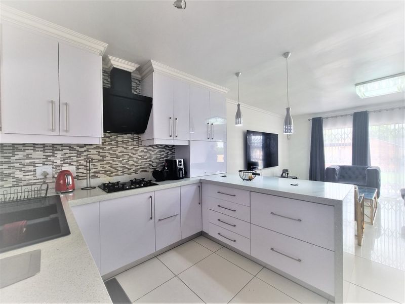 Modern open-plan kitchen featuring white gloss cabinetry, stone countertops, a gas hob, and a stylish mosaic backsplash, seamlessly flowing into the living area.