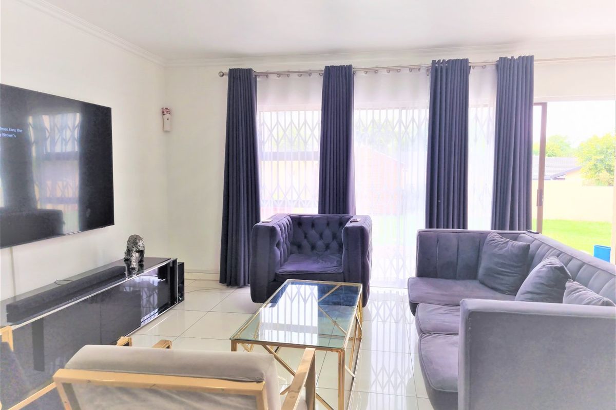 A bright living room featuring large format floor tiles, a skylight, and a sliding glass door with security gate leading to the garden.