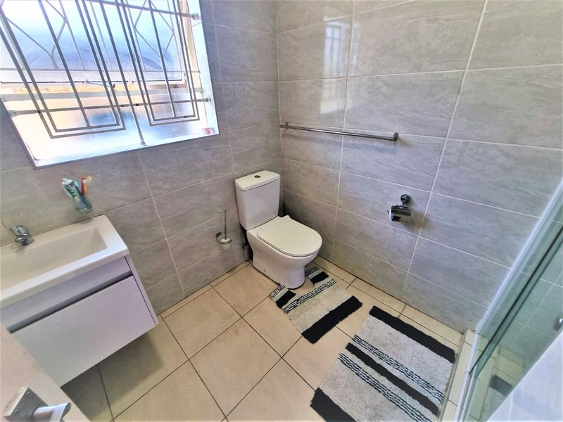 A clean, modern bathroom featuring tiled walls and floors, a vanity cabinet with basin, a toilet, and a glass-enclosed shower.